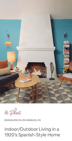 A living room with modern blue and red furniture, a wooden coffee table, and a tall stack of neatly piled books.