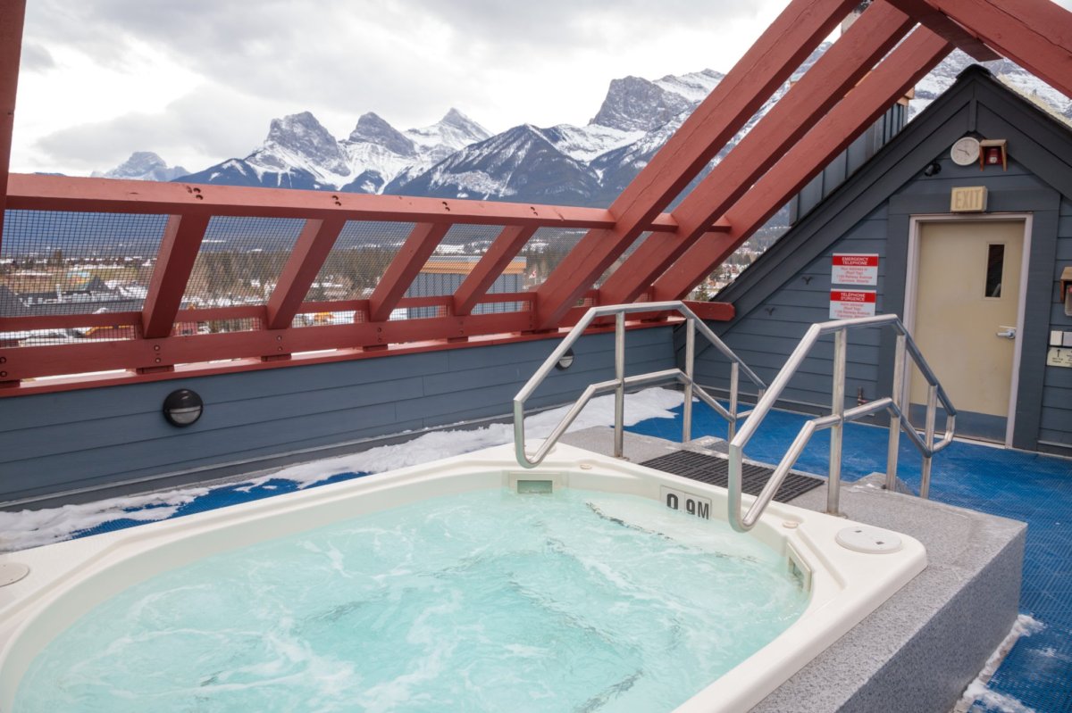 A rooftop hot tub is centrally positioned, offering stunning views of the surrounding mountains. The area is enclosed with a wooden frame and features a slanted roof, allowing for light to filter through while providing a serene space to relax.