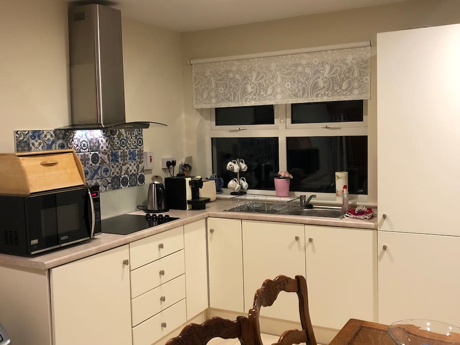 Modern kitchen with electric hob, microwave combo oven, Nespresso coffee machine, fridge, kettle and toaster.