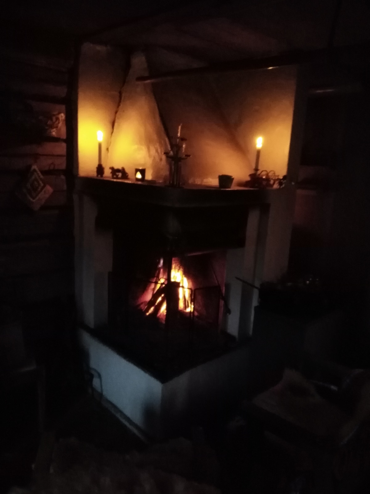 A rustic fireplace is featured, with a fire gently flickering inside. Two candles emit a soft glow, illuminating the surrounding area. The mantel holds decorative items, contributing to the cozy atmosphere of the space.