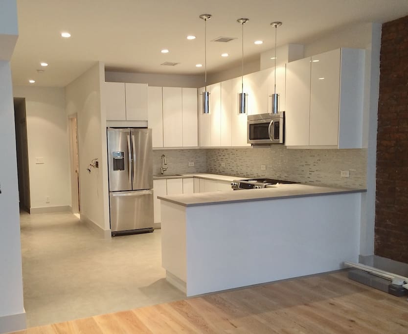 kitchen features bright white lacquer cabinets, quartz countertop, high end stainless steel appliances, undercabinet lighting, and beautiful glass and steel mosaic backsplash
