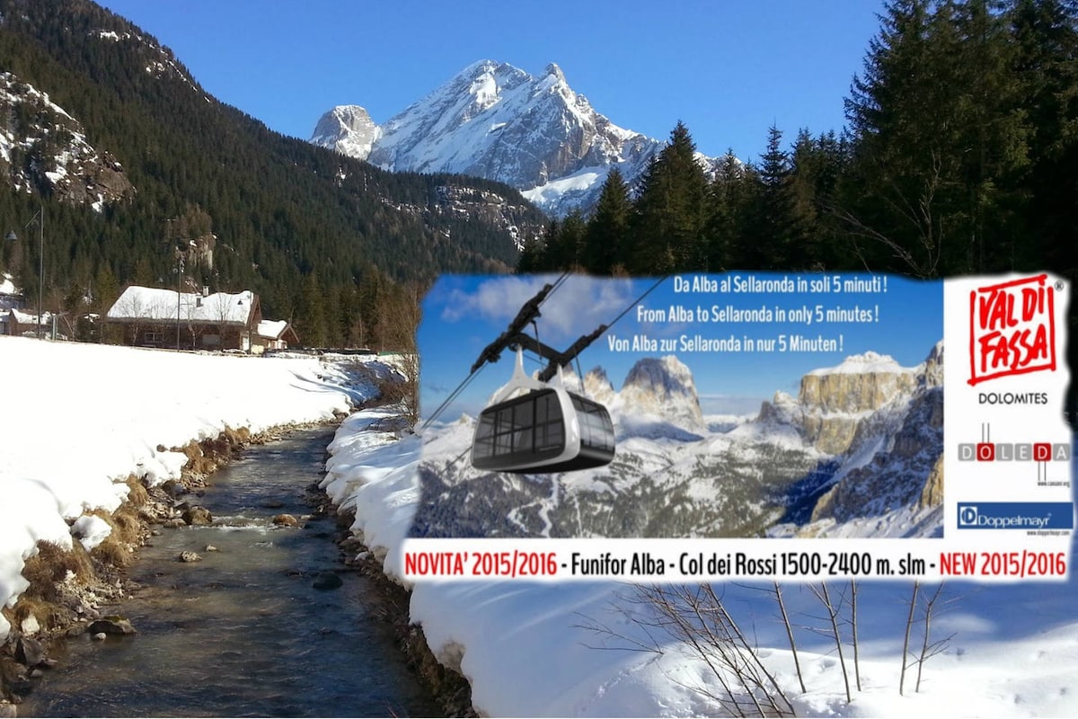 A snow-covered landscape features a flowing river, with majestic mountains in the background. A ski lift stands ready for transportation, connecting the valley to various ski slopes. The scene embodies the charm of the Dolomites, with clear blue skies and snow-laden peaks.