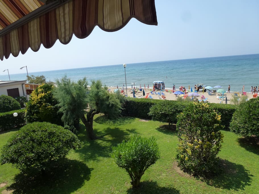Vista dal balcone dell'appartamento: giardino condominiale, spiaggia e mare.