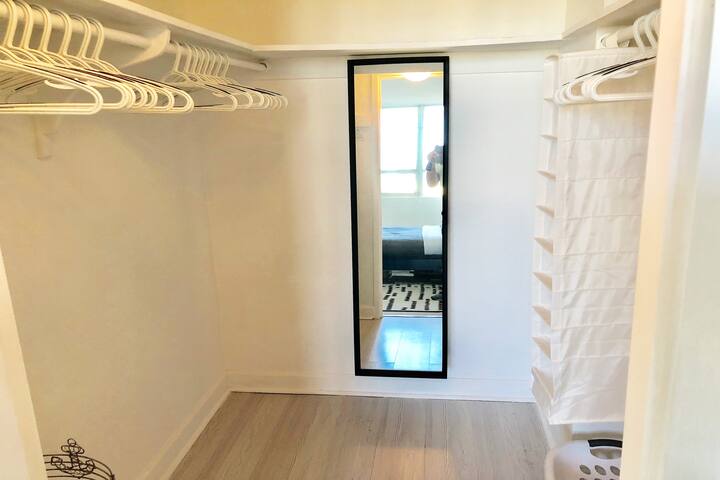 Walk-in closet with tall mirror, clothes hangers, shelves, iron and ironing board.