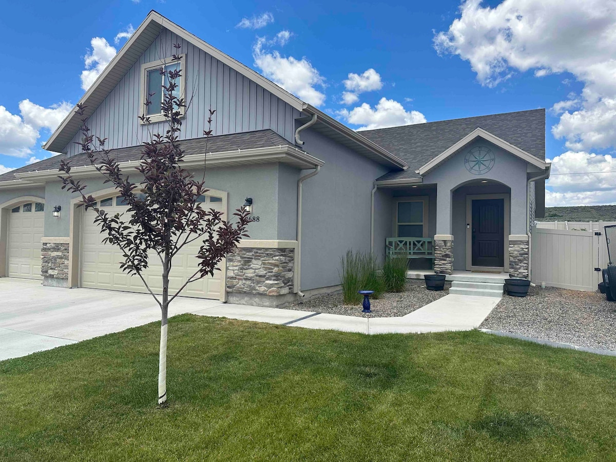 A modern, two-story home is presented with a welcoming front porch and decorative stone accents. A manicured lawn frames the pathway leading to the entrance. The driveway provides access to double garage doors, and a small tree adds a touch of greenery.