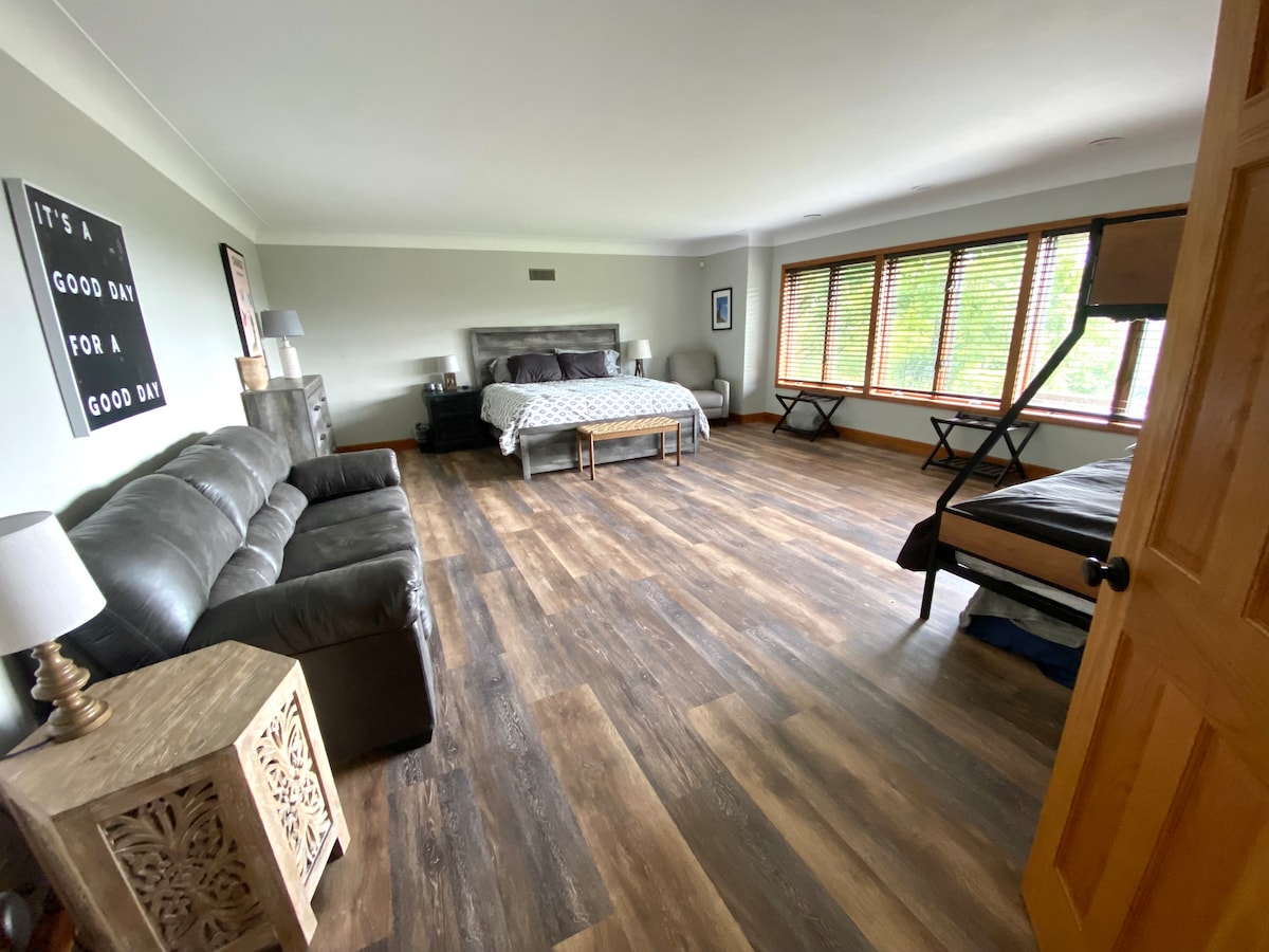 A room with a view on the main level.  Double entry doors  with a King bed, twin over full bunk bed, framed floor mattress, and a sofa sleeper.  This room is over 400 square feet with many windows 