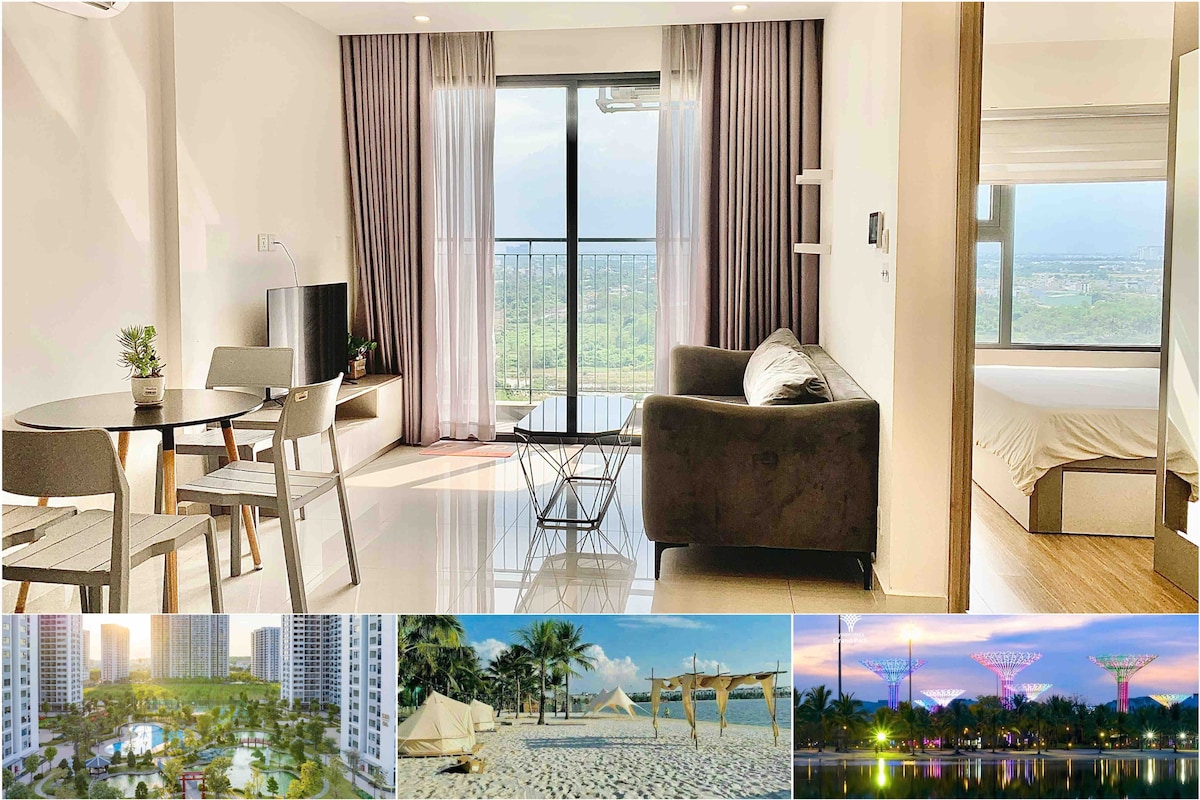 A bright living area features a comfortable sofa and a round dining table set for four, with large windows that showcase views of the surrounding greenery. Soft curtains frame the view, offering a sense of openness and light.