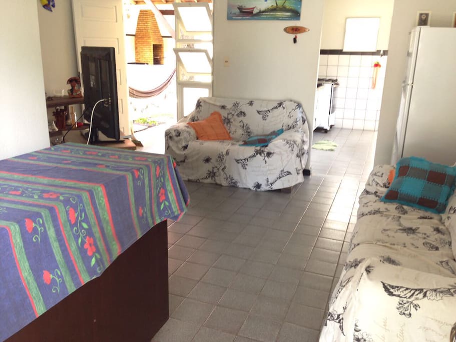 Visão da sala quando se entra na casa, acesso à cozinha, ao quarto externo, à churrasqueira e à área de serviço