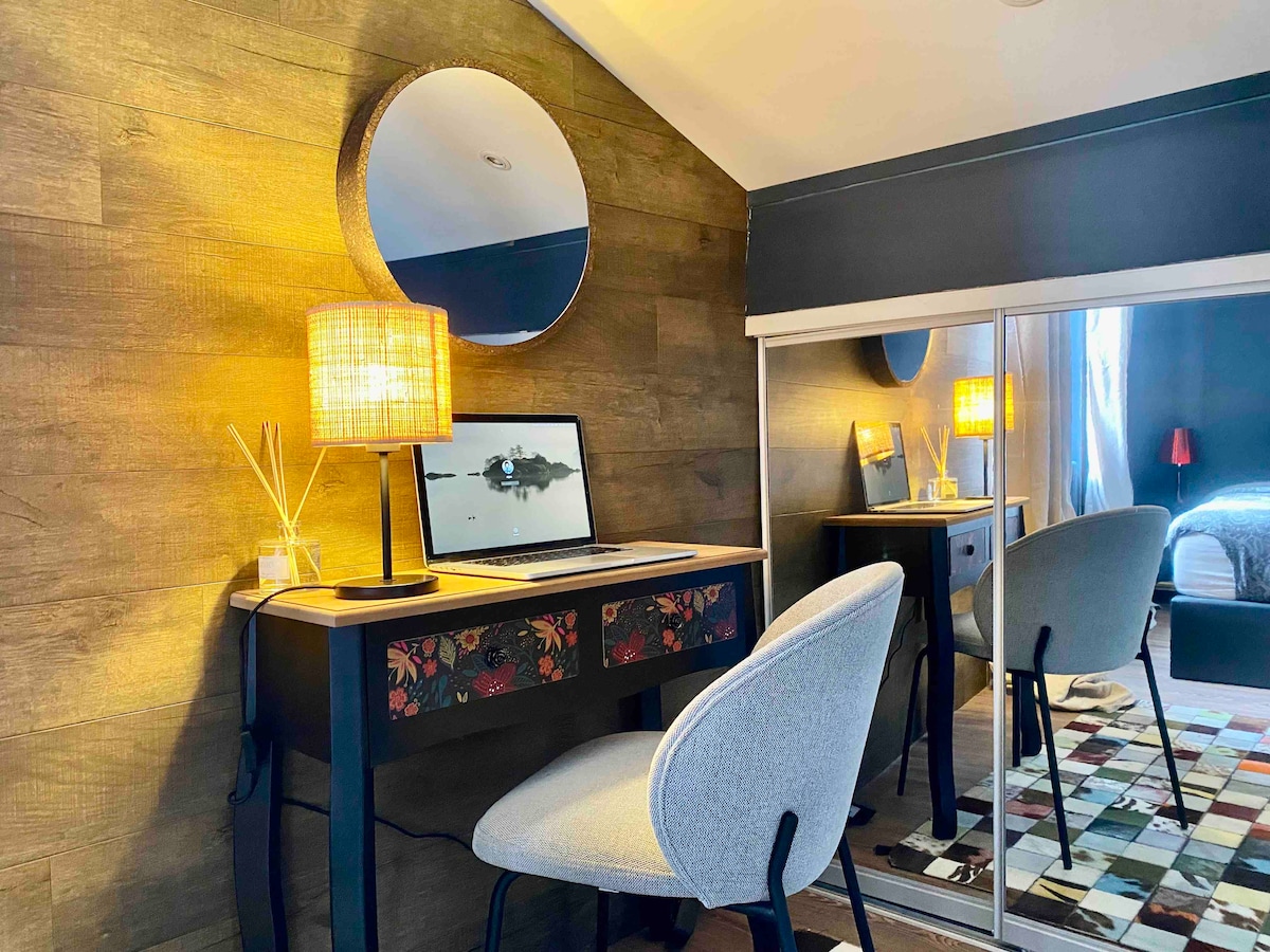A dedicated workspace features a decorative desk with floral accents and a comfortable chair. A round mirror reflects soft lighting from a lamp, while a laptop sits open atop the desk. A wardrobe with mirrored doors is visible in the background, enhancing tranquility.