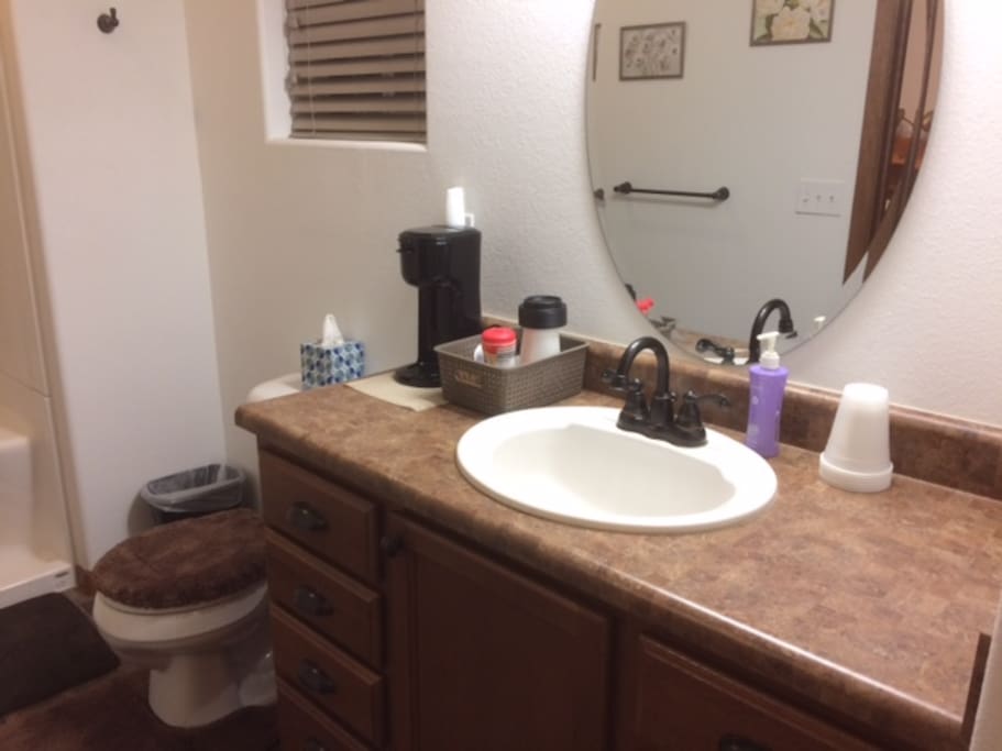 Bathroom counter with K-cup coffee maker, coffee go cups, variety of K-cup coffees, teas, sugar and creamer.
