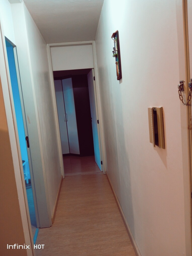 A narrow hallway is visible, featuring light-colored walls and a smooth floor. A door on the left leads to a room beyond, while another door on the right remains closed. Wall decor and a doorbell are mounted beside the entrance, contributing to the functional layout.