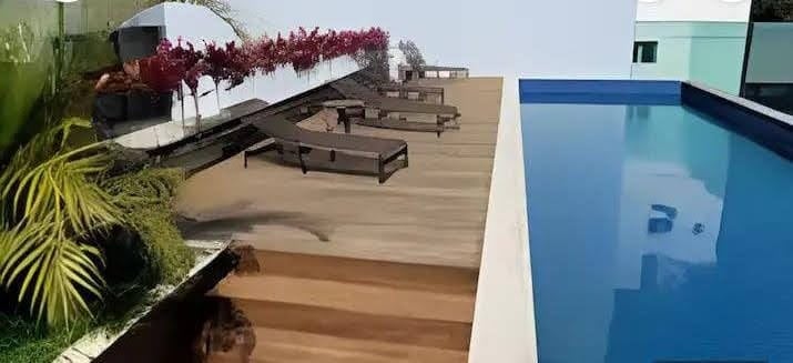 An inviting outdoor area features a clear blue pool alongside wooden decking. Comfortable lounge chairs are arranged for relaxation, and decorative plants add a touch of greenery to the space. The setting offers a tranquil atmosphere for leisure and enjoyment.