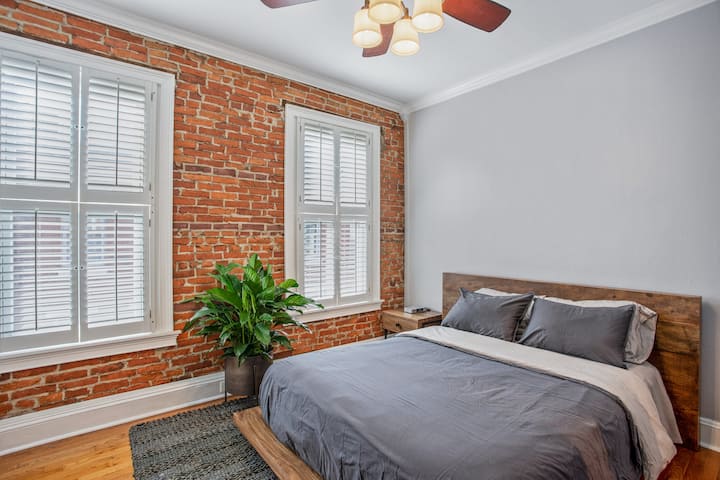 غرفة نوم رئيسية بسرير بحجم كوين مع مرتبة سيمونز بيوتيست الجديدة. أيضًا راديو iPhone يعمل بالساعة وطاولة بجانب السرير ومكتب.