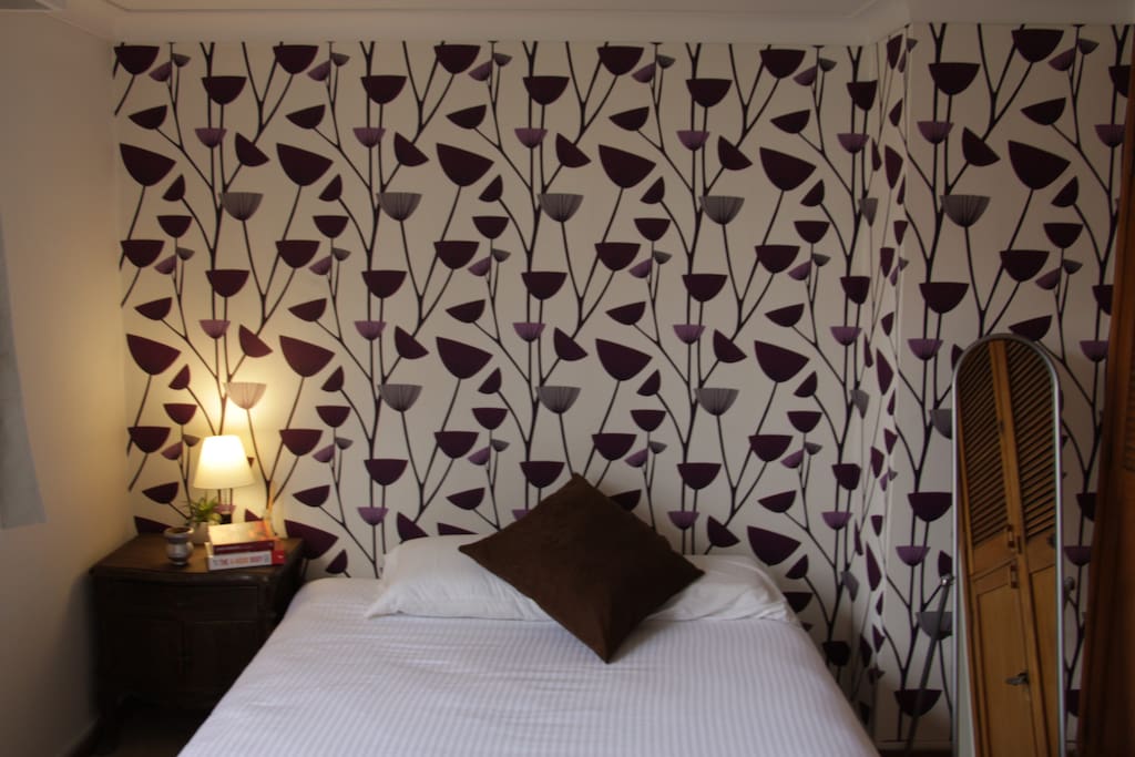 View of bed and wallpaper with night stand.