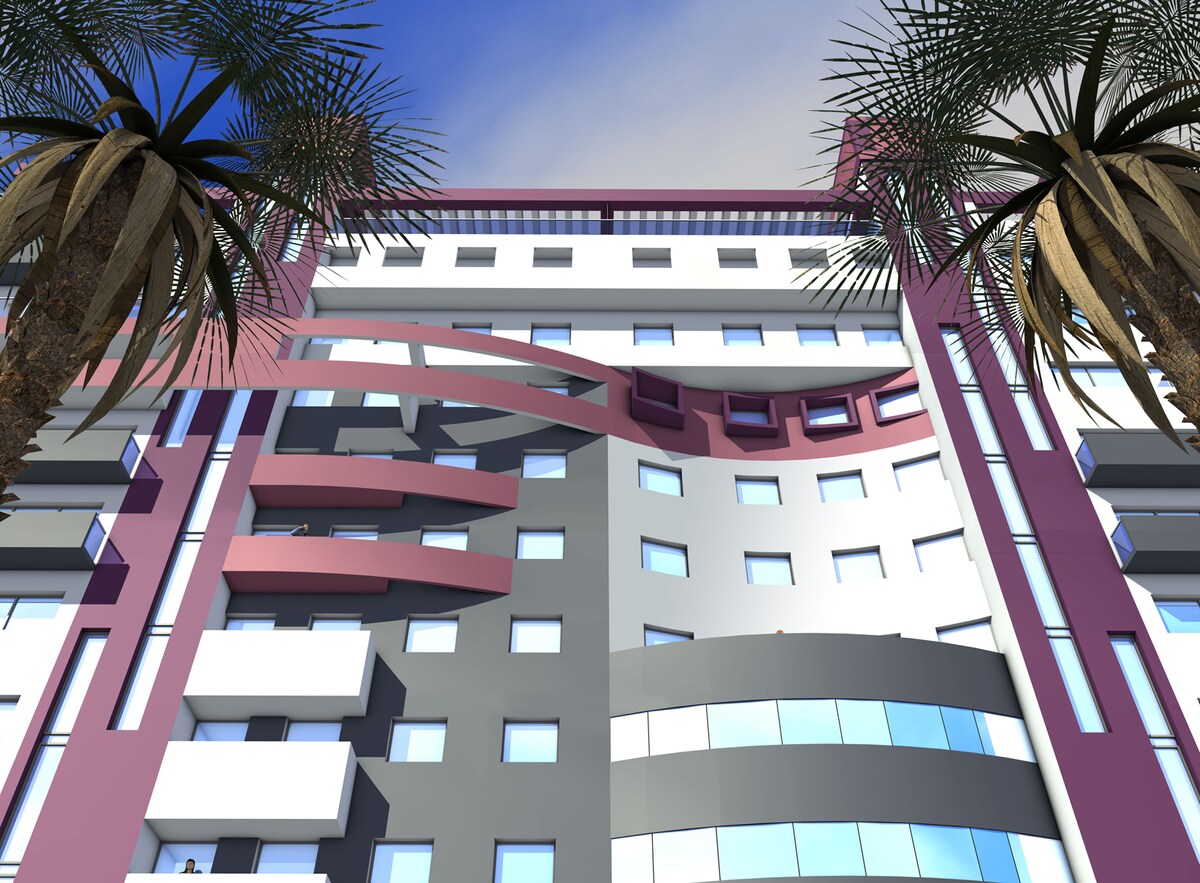 The exterior of a modern apartment building features a blend of white, grey, and pink façades with multiple balconies. Palms frame the scene, while large windows reflect the sky above, creating a vibrant urban appearance.
