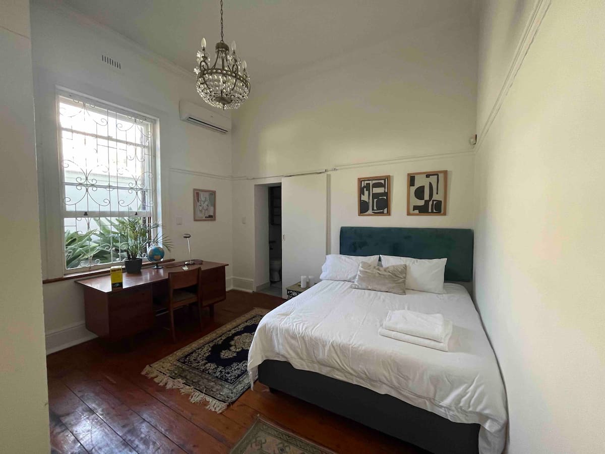 En-suite queen bedroom with desk and chandelier at Utopia co-living in Fresnaye, Cape Town
