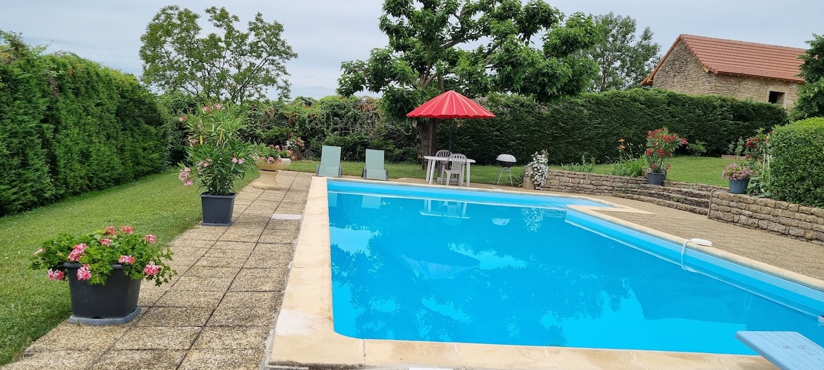 A private pool is situated in a landscaped garden, surrounded by lush greenery and flowering plants. Comfortable lounge chairs are positioned by the poolside, while a red umbrella offers shade. The area is paved, providing ample space for relaxation and enjoyment.