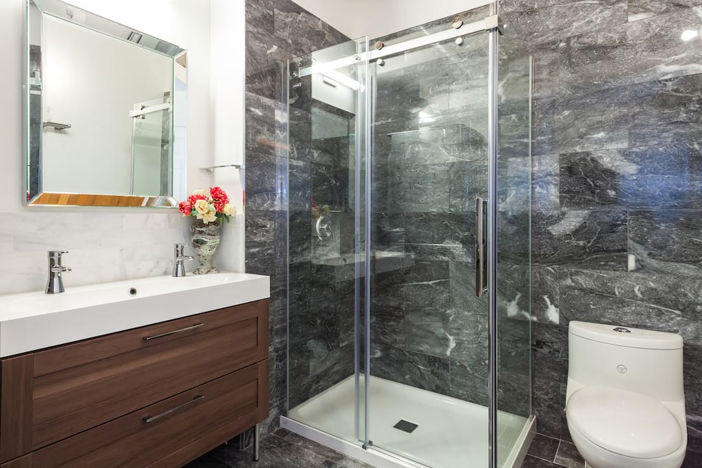 Marble floors and walls, corner walk-in shower with glass sliding bypass entry and grey gloss stacking washer & dryer definitely make this bathroom luxurious.