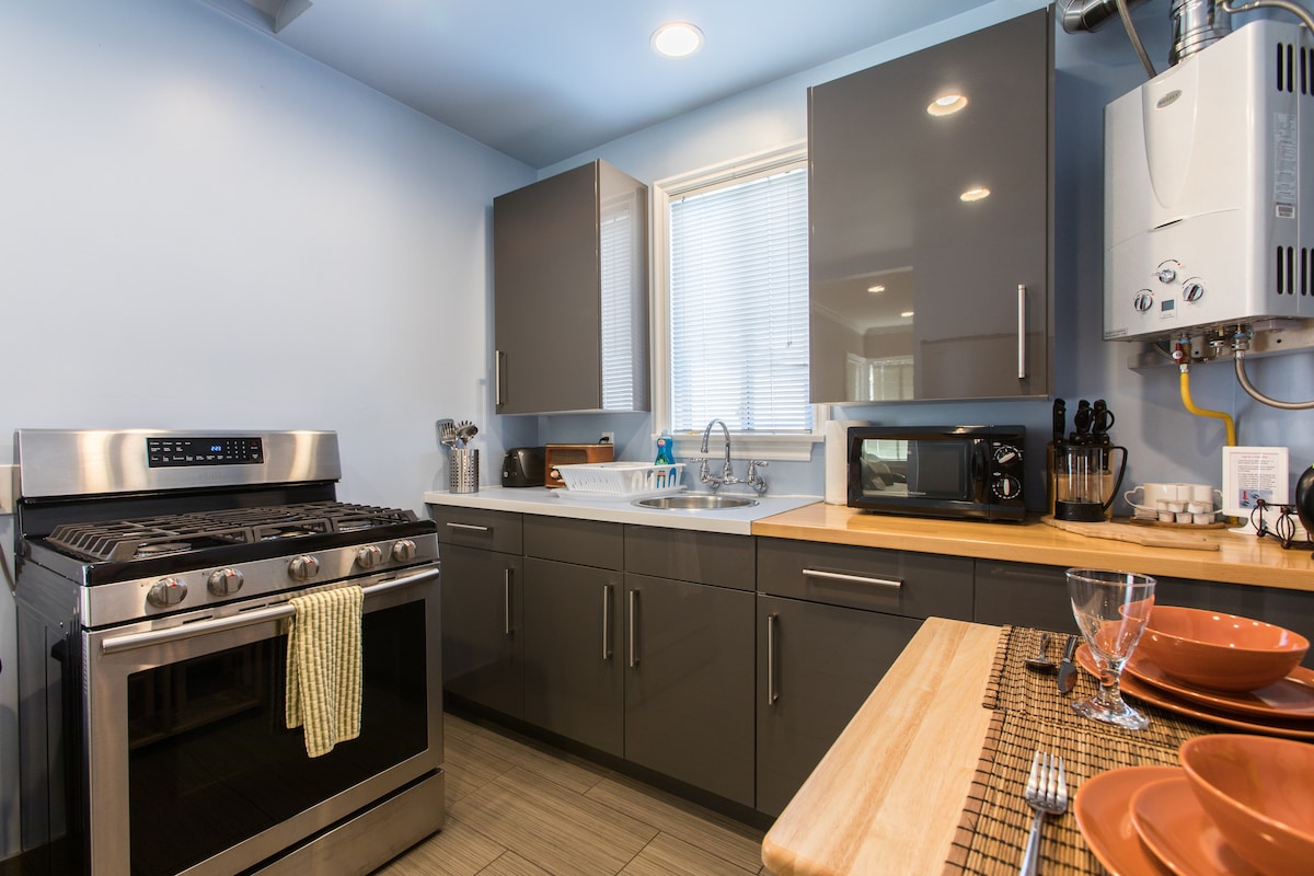 The kitchen features sleek gray cabinetry and modern appliances, including a stainless steel gas stove and a convenient sink area. Natural light enters through the window, illuminating the counter space, which is equipped with utensils and a coffee maker.