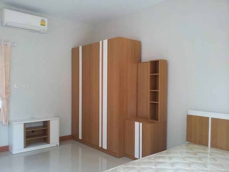 A neat bedroom setup is showcased, featuring a spacious wardrobe with white accents, a storage unit with open shelves, and a low-profile TV stand. A light-coloured bed frame is positioned against the wall, complemented by glossy tiled flooring and minimalistic decor.