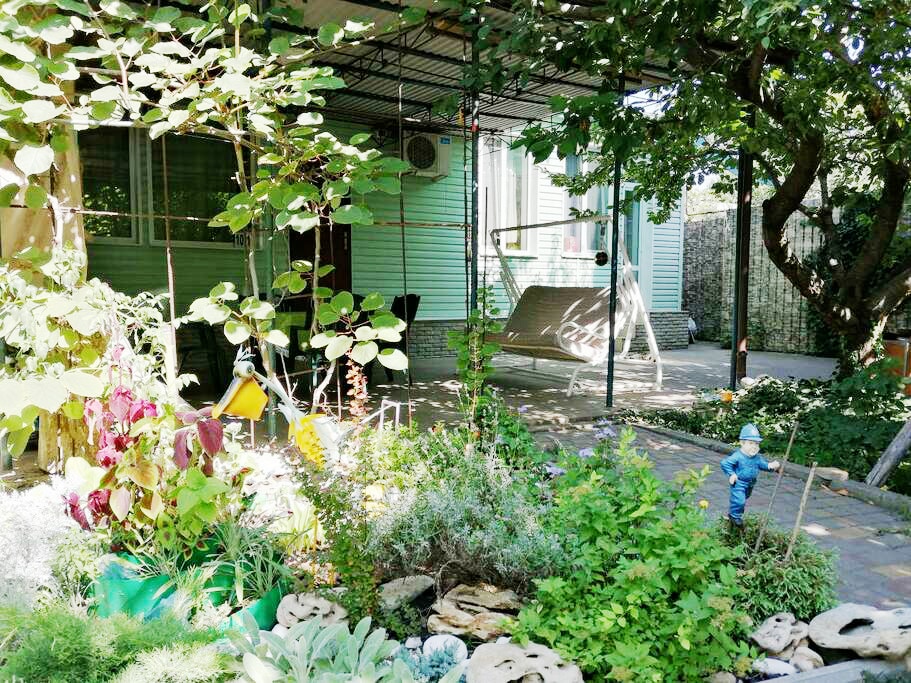 A green space is highlighted with a variety of plants and decorative elements. A swing hangs from a structure near a shaded terrace. A small garden gnome adds a whimsical touch, while a paved area offers a relaxing outdoor environment.