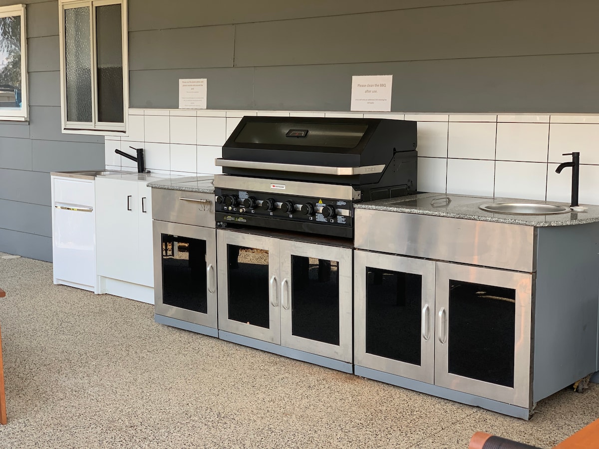 The outdoor kitchen area is equipped with a large barbecue grill, stainless steel cabinetry, and a countertop with sinks. A refrigerator is also present, providing convenient access to food and drinks while enjoying outdoor entertaining.