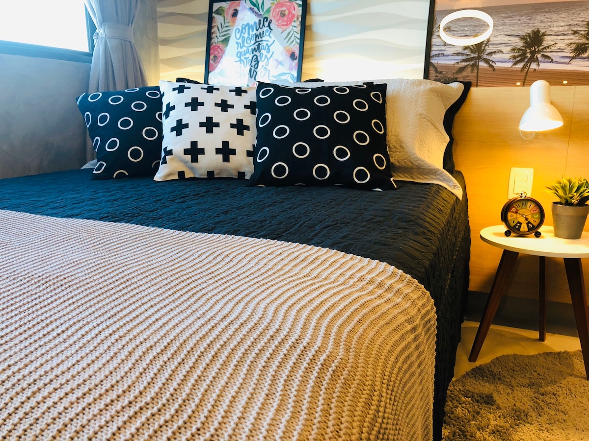 A cozy sleeping area is present, featuring a spacious bed adorned with patterned pillows and a textured blanket. A bedside table with a lamp offers additional lighting, and decorative wall art adds visual interest to the room.