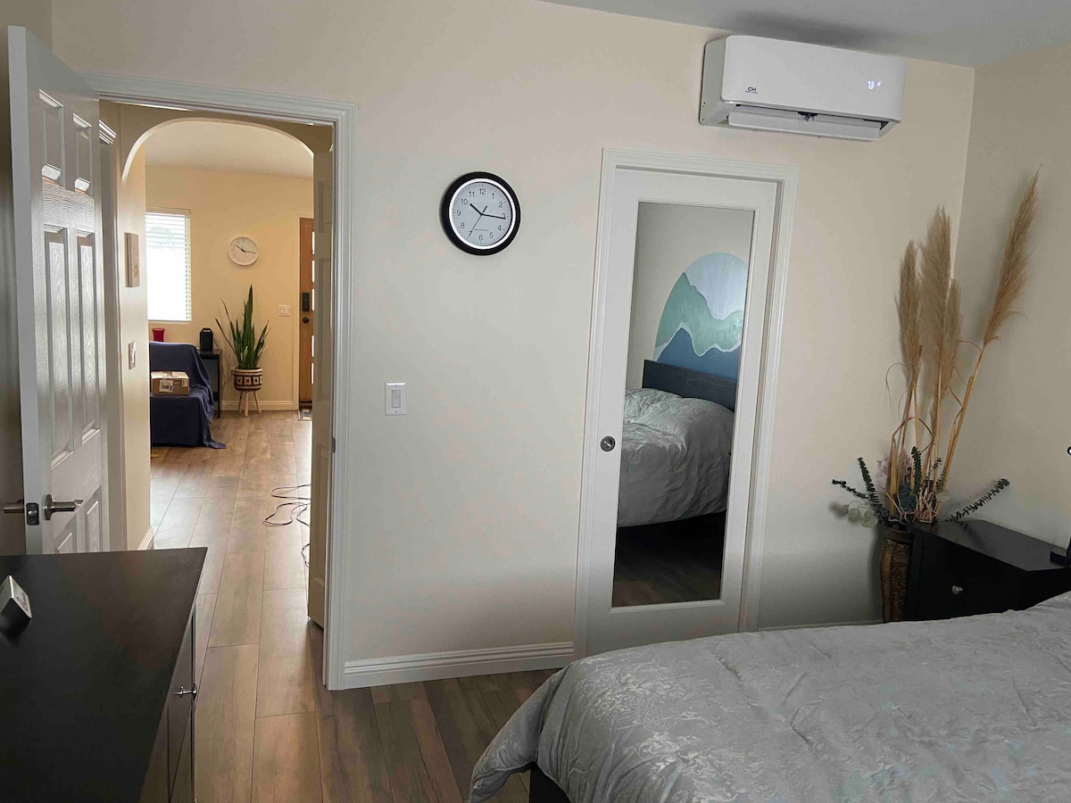 La puerta de tamaño sólido separa el dormitorio de las áreas de estar.  El dormitorio tiene colchón queen, mesitas de noche, vestidor de 8 cajones y silla de estar.  El vestidor está detrás de la puerta corrediza con espejos