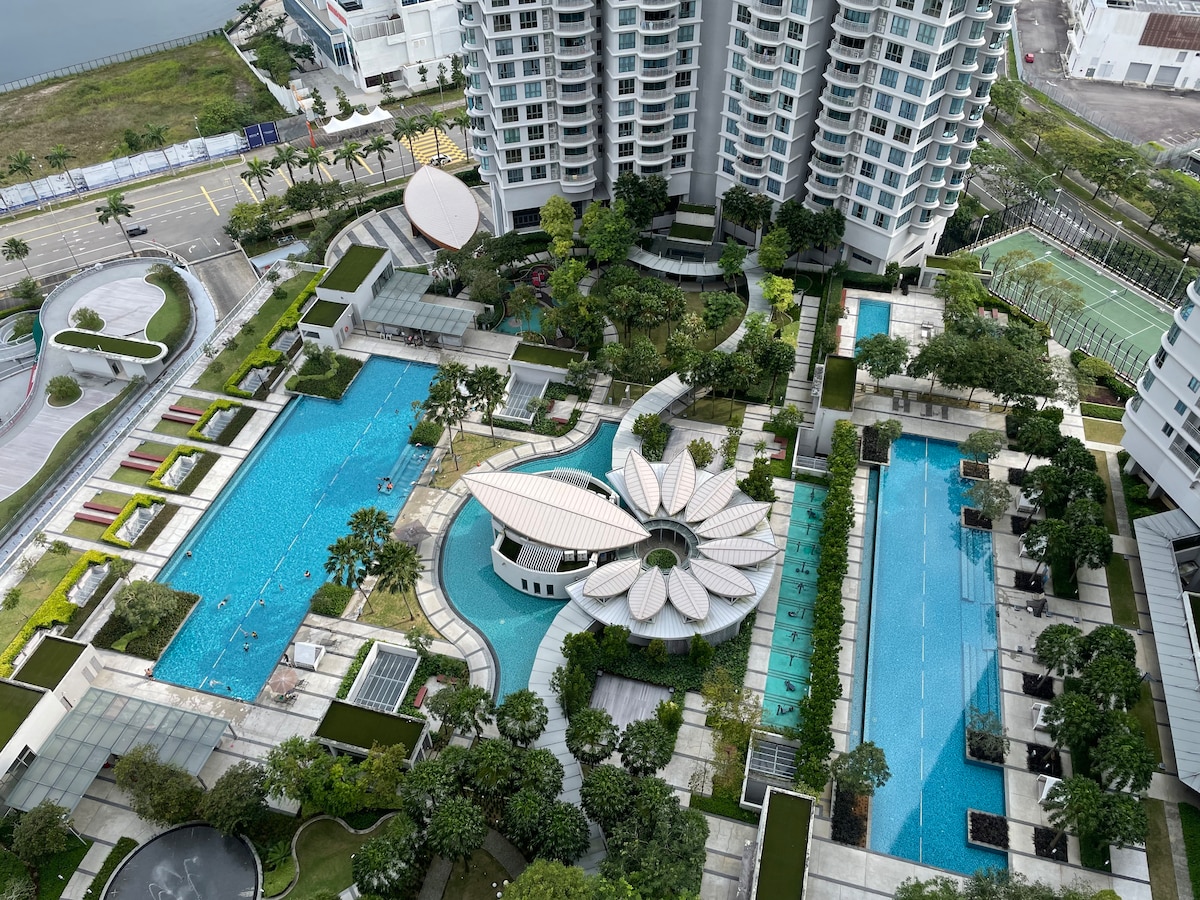 An aerial view of the condominium complex showcases a sprawling landscape of swimming pools, gardens, and recreational areas. The pools are surrounded by neatly arranged greenery and modern architecture, enhancing the inviting environment of the community amenities.