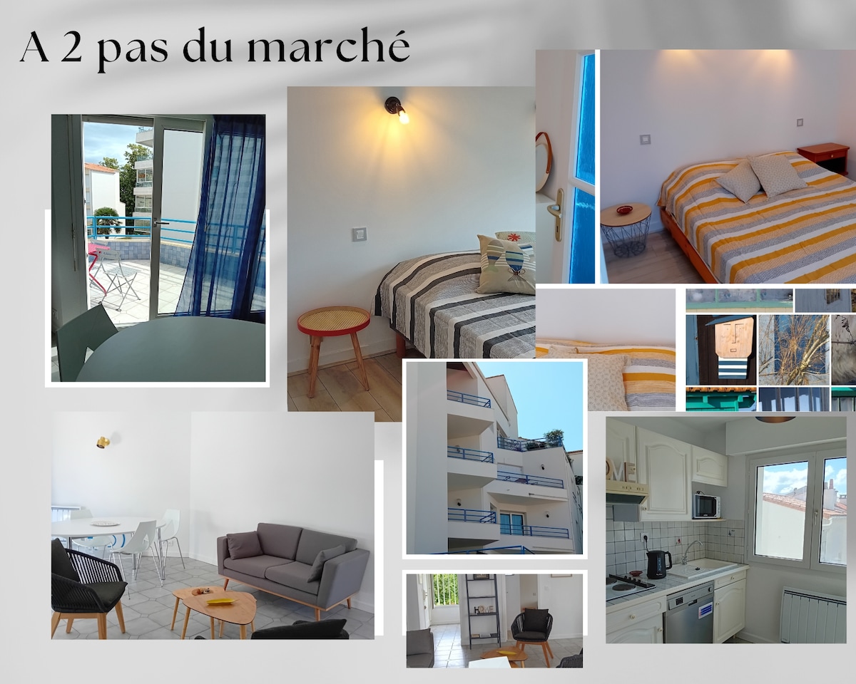 A light-filled apartment features a mix of cozy and modern furnishings, including a spacious bed with a striped blanket, a comfortable sofa, and a dining area illuminated by natural light. A view of the balcony is visible, enhancing the overall openness of the living space.