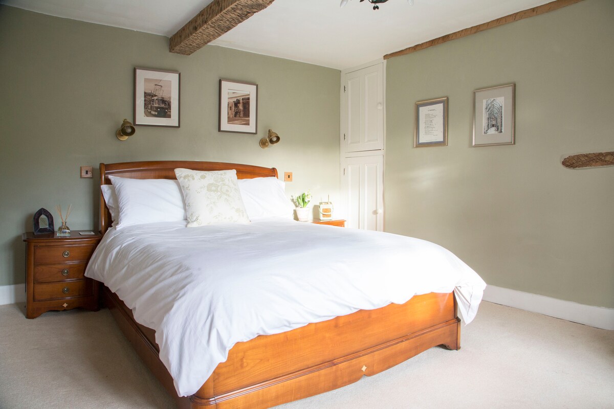 A spacious bedroom is furnished with a king-size sleigh bed featuring Egyptian cotton bedding. Soft, neutral tones decorate the walls, complemented by wooden accents and bedside lamps. A wardrobe and nightstand are positioned beside the bed, providing essential storage and decorative touches.
