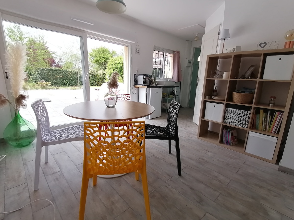 A dining area features a round table surrounded by four uniquely designed chairs in white, black, and yellow. Natural light fills the space through large glass doors leading to an outdoor terrace, enhancing the open and airy atmosphere.