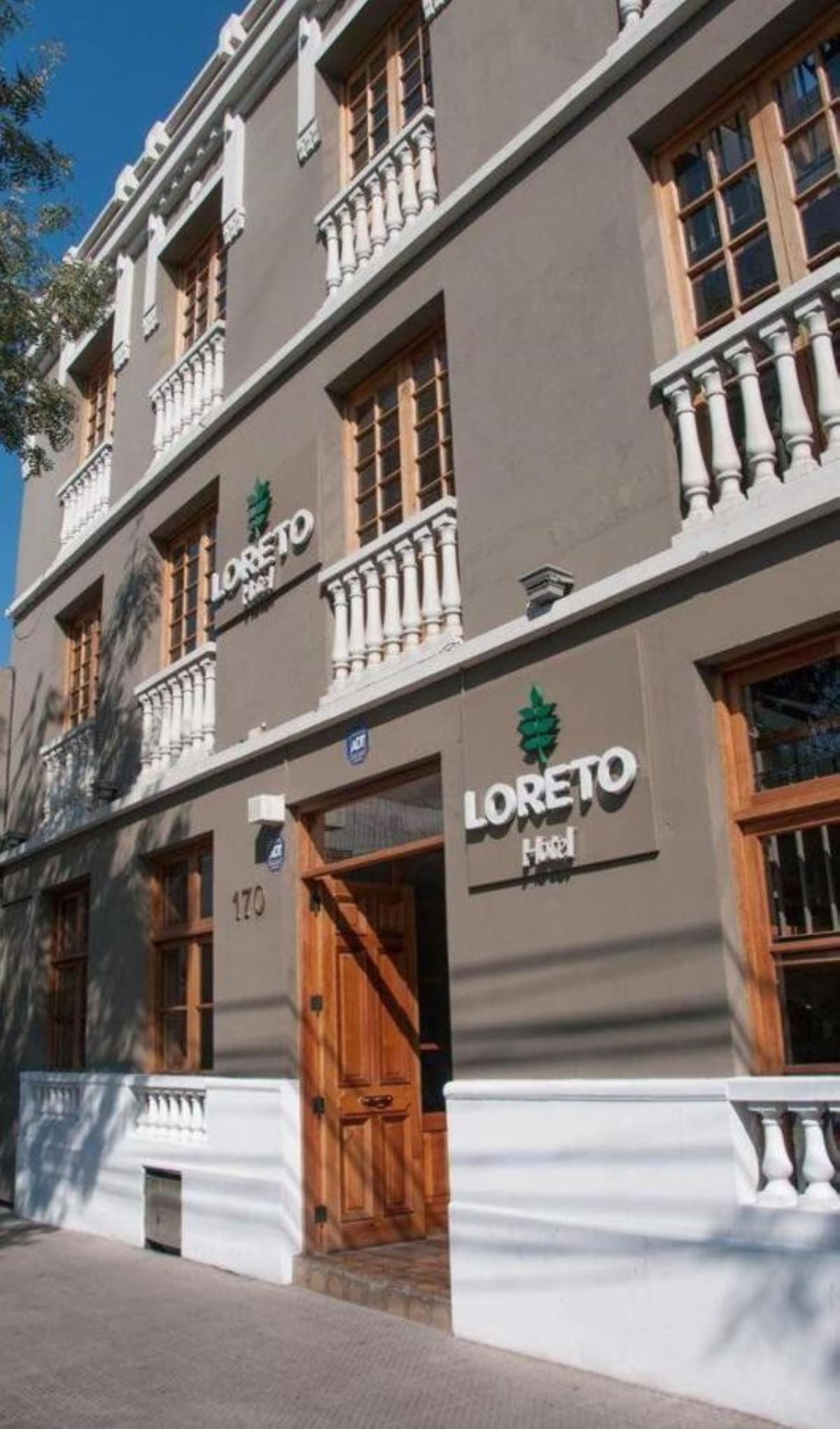 The exterior of Hotel Loreto features a charming three-story building with a muted grey facade and wooden windows. Ornate balconies are visible, adding architectural interest. The entrance is framed by a wooden door and signage, offering a welcoming first impression.