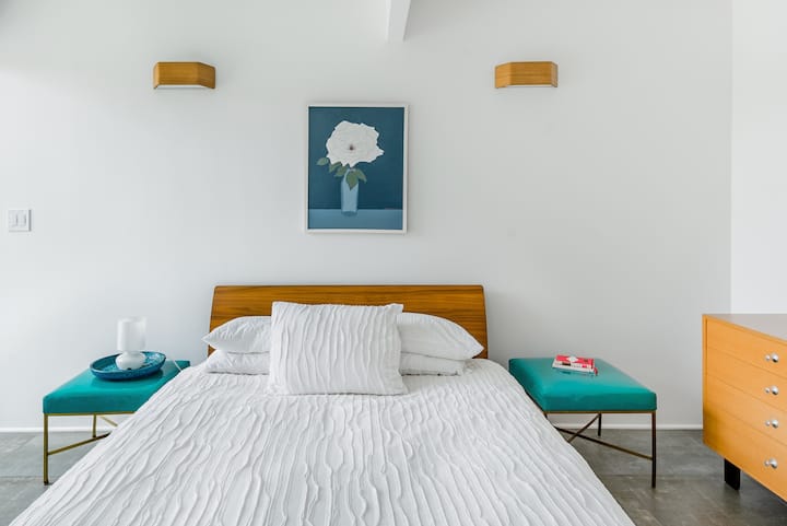 - Relax in a comfortable bed with crisp white linens and warm mid century design
- Teal benches and matching decor add a fresh pop of color to the serene setting
- Enjoy a peaceful night’s rest in this bright and beautifully styled retreat