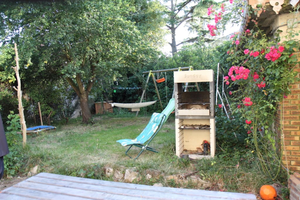 Jardin avec une terrasse, un barbecue à charbon de bois, une balançoire pour enfants avec toboggan