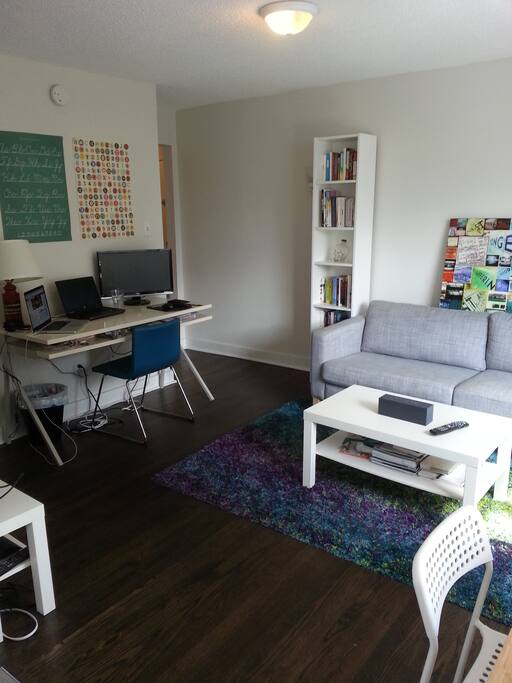 Bright main space with large firm comfy couch (could be used as another bed), large desk, 32-in TV with cable, and small dining table.