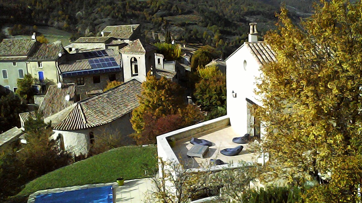 A serene view features a spacious terrace with lounge chairs overlooking lush greenery and rooftops. The surrounding landscape is adorned with autumn foliage, and solar panels are visible on the nearby rooftops, reflecting an eco-friendly approach.