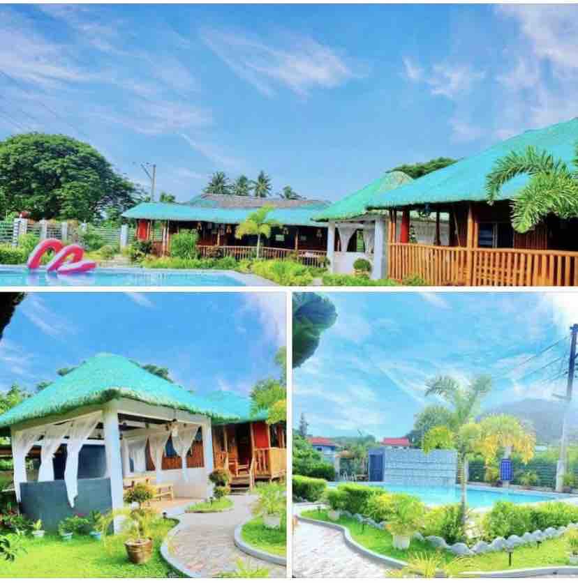 The image displays two nipa huts with green thatched roofs, surrounded by lush greenery and a swimming pool. A gazebo is shown with open sides, offering views of the garden. The bright blue sky enhances the inviting outdoor setting.
