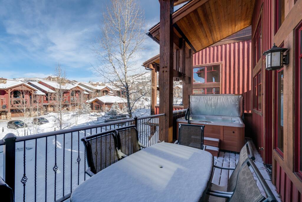 A table with 5 chairs and a grill amid a bubbling hot tub create a great outdoor space