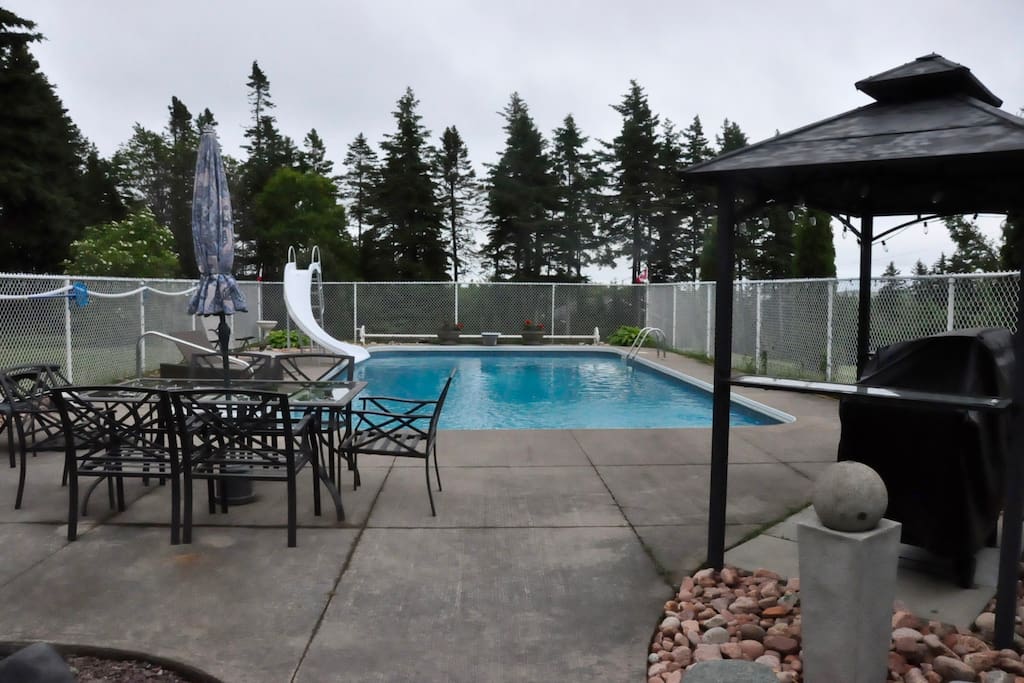 Pool area with bbq, table set with umbrella, pool seating.