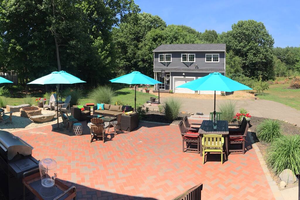 Large patio, fire pit, grill, dining table, couches, umbrellas for shade.