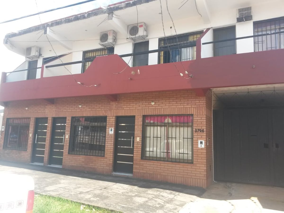 A two-story building features a brick facade and large windows with black bars. Several entrance doors are visible, flanked by air conditioning units. A covered entrance leads to a dark double door, creating an inviting access point.
