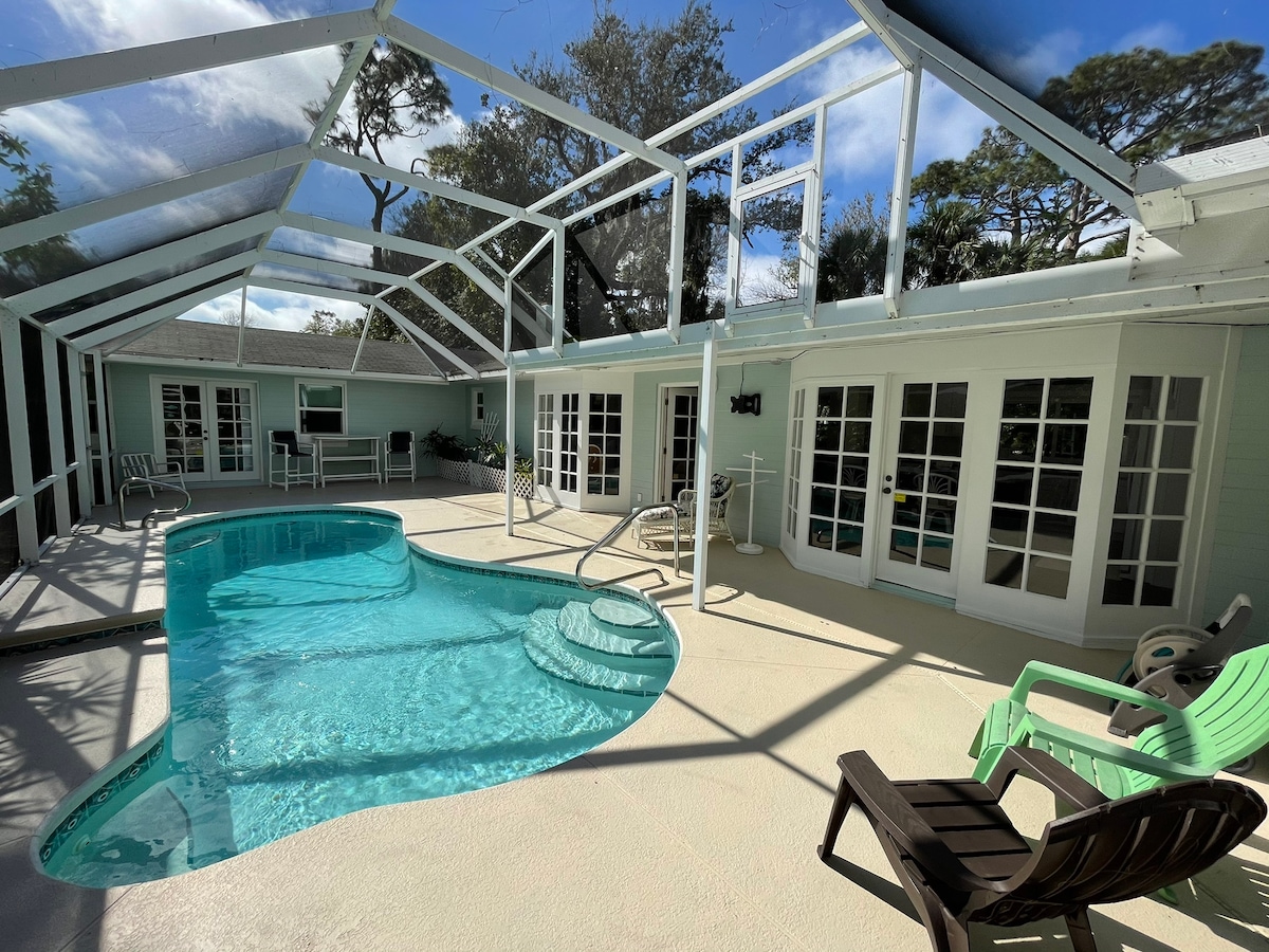 A screened-in outdoor area features a private swimming pool with gentle steps leading in. Several lounge chairs in varying styles are arranged around the pool. Large glass doors from the adjacent rooms offer abundant natural light and visible connections between indoor and outdoor spaces.
