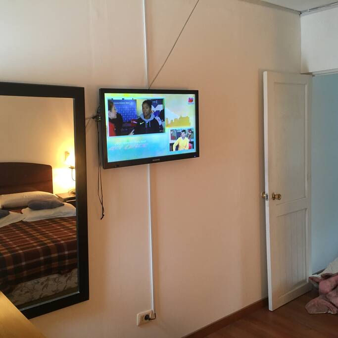 Vista parcial de dormitorio con cama matrimonial, tv cable y espejo