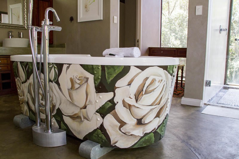 A uniquely designed bathtub features intricate floral patterns, creating a focal point in the spacious bathroom. Natural light filters through nearby windows, illuminating the room's neutral tones. A towel is neatly placed on the edge of the tub, adding to the organized appearance.