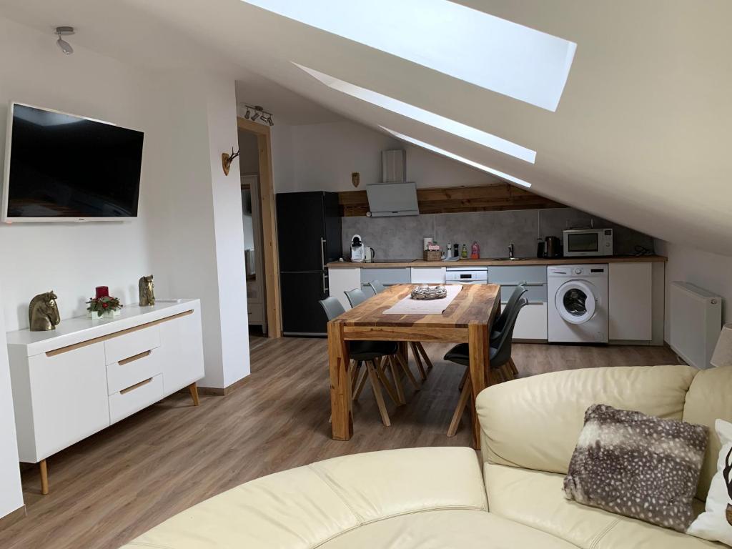 A modern living area features a spacious sectional sofa, a wooden dining table with chairs, and an open kitchen equipped with essential appliances. Skylights illuminate the room, emphasizing the contemporary decor and warm wooden accents.