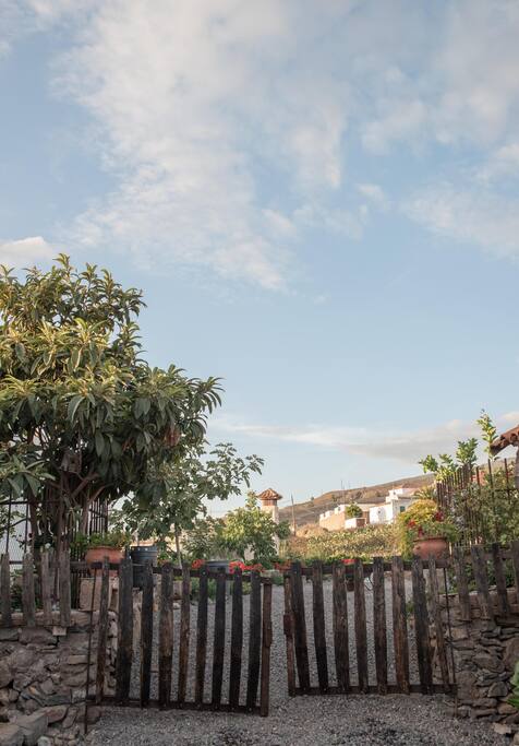 Verja hecha a partir de tablas de barrica que conduce a la parte trasera del jardín, donde se hallan un baño una zona techada y amueblada a modo de cocina y con chimenea y brasa.