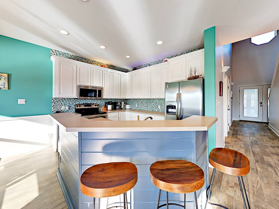 Open kitchen with stocked white cabinetry, stainless steel appliances, and a breakfast bar for 3.