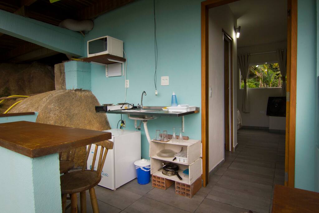 Mini cozinha com frigobar, microondas, pia, utensilios de cozinha e fogao eletrico com 2 bocas