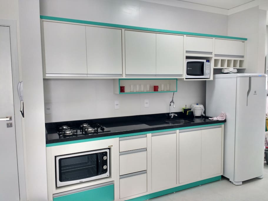 Cozinha com louças, talheres, geladeira, forno elétrico, microondas, sanduicheira, torradeira, liquidificador